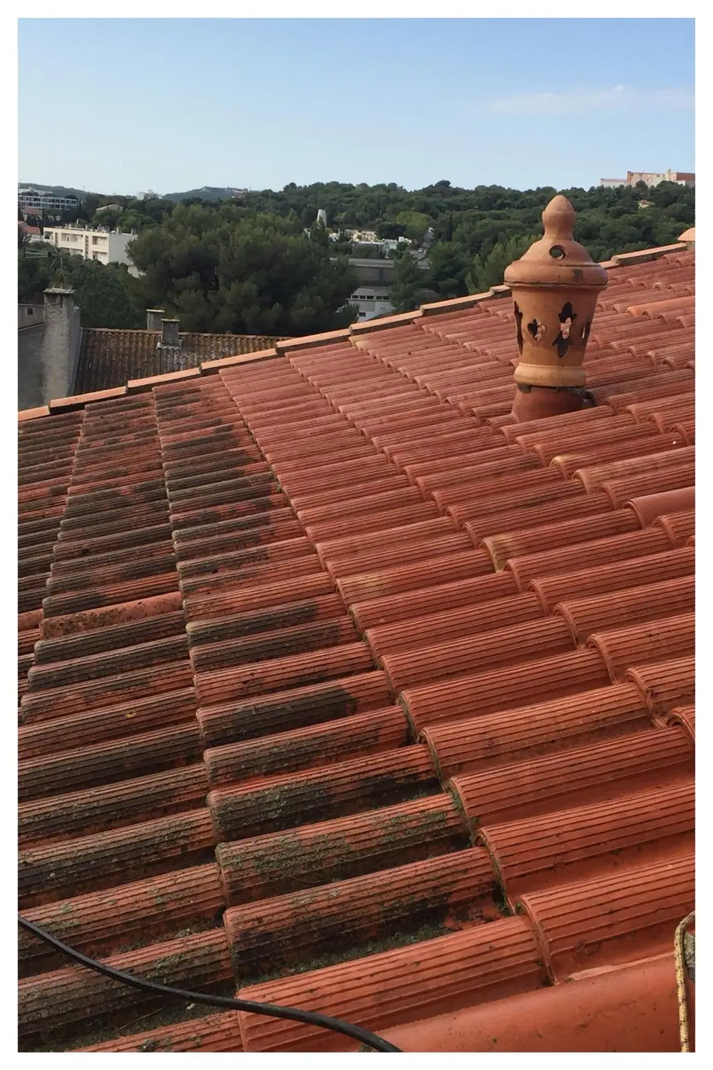 Toiture en tuiles romanes couvertes de mousse, épi de faîtage en terre cuite ajourée